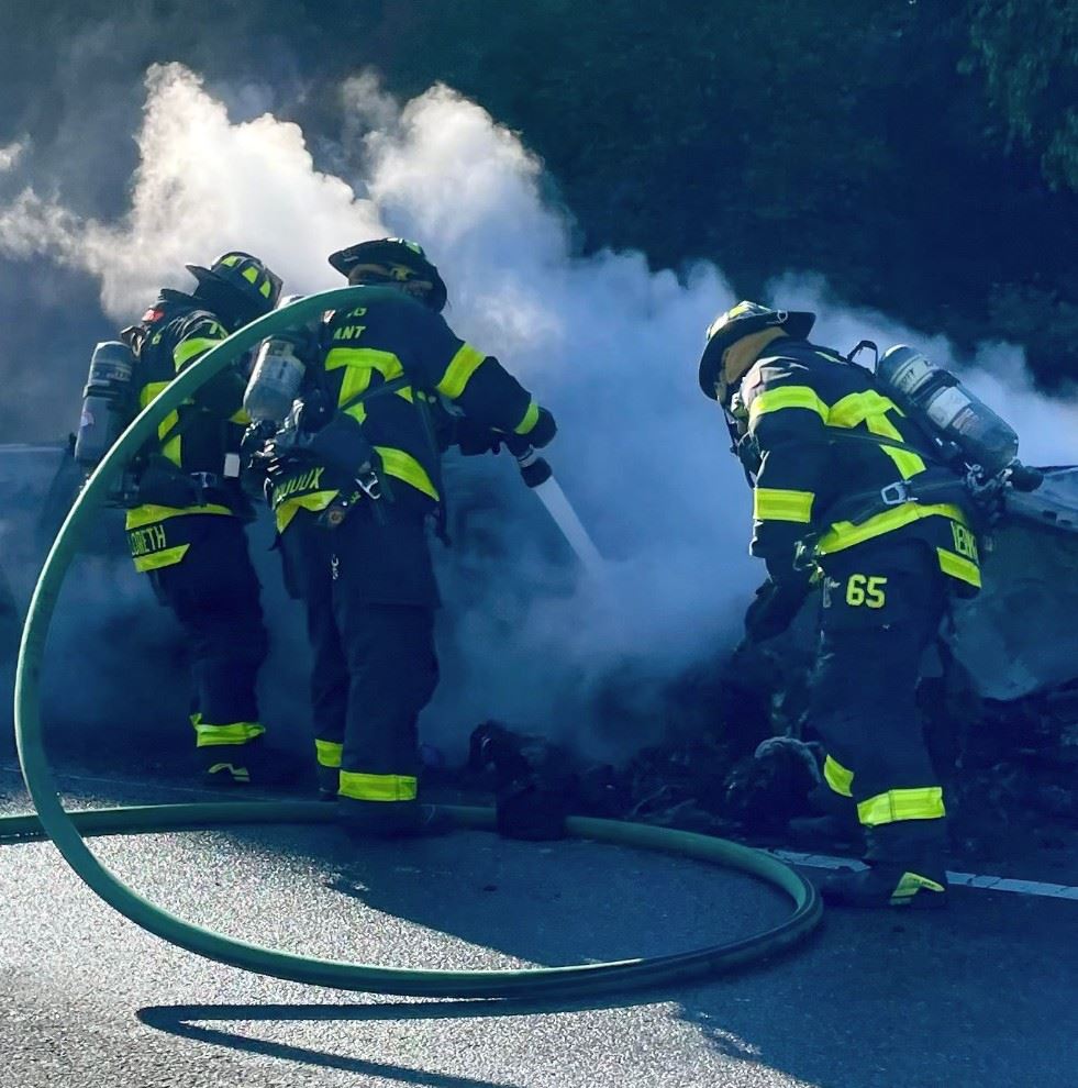 Three firefighters spraying water on a vehicle fire.