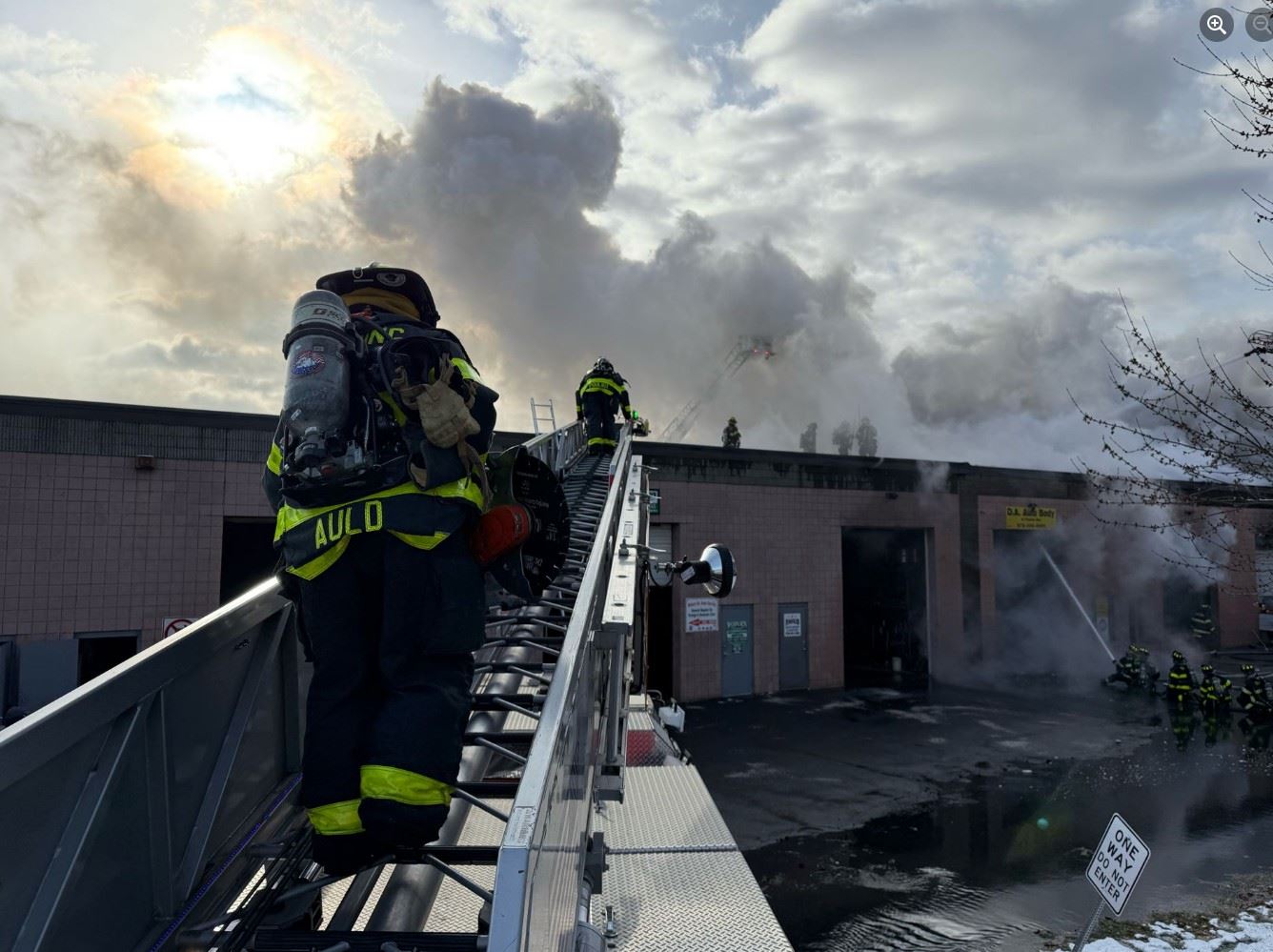 A firefighter climbing the Reading Fire Department ladder truck to the roof of building on fire.